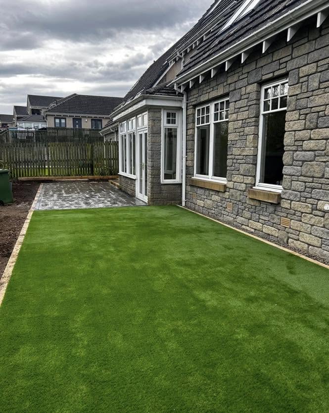Artificial lawn beside a stone-clad house with slab patio